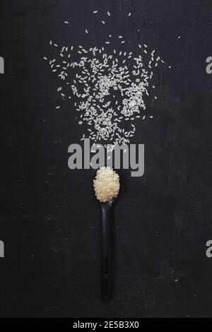 Gesunder Lebensstil. Schwarzer Löffel mit weißem Reis auf einem Holztisch. Weißer Reis im Löffel auf schwarzem Hintergrund. Kopierraum. Stockfoto