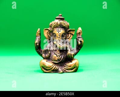 Statuette eines Elefanten Ganesha aus Messing auf grünem Hintergrund. Ganesha, auch bekannt als Ganapati und Vinayaka, ist einer der bekanntesten und bekanntesten Stockfoto