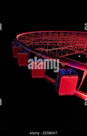 Blick auf das rote Riesenrad bei Nacht von unten, mit Mond am Himmel. Stockfoto