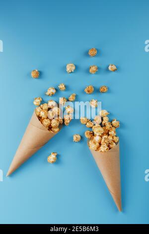 Karamell Popcorn in einem Papierumschlag auf blauem Hintergrund. Köstliches Lob für das Ansehen von Filmen, Serien, Cartoon. Freier Speicherplatz, Nahaufnahme. Minimalis Stockfoto