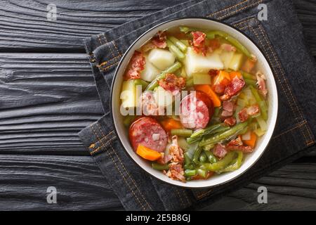 Hausgemachte Suppe aus grünen Bohnen, Kartoffeln, Lauch, Karotten mit Würstchen und Speck aus der Nähe auf einem Teller auf dem Tisch. Horizontale Draufsicht von oben Stockfoto