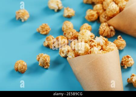 Karamell Popcorn in einem Papierumschlag auf blauem Hintergrund. Köstliches Lob für das Ansehen von Filmen, TV-Serien, Cartoons. Freier Speicherplatz, Nahaufnahme. Minimalisti Stockfoto