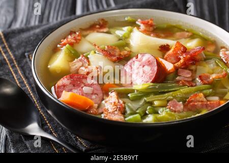 Hausgemachte Suppe aus grünen Bohnen, Kartoffeln, Lauch, Karotten mit Würstchen und Speck aus der Nähe auf einem Teller auf dem Tisch. Horizontal Stockfoto
