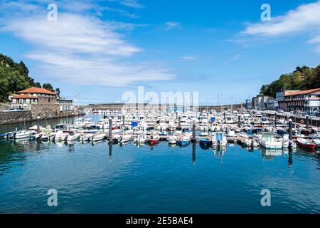 Weiße Segelboote in Mutriku Hafen und Altstadt, Baskenland, Spanien. Blick auf die bunten Boote, die am Yachthafen von Motrico mit Blick auf das kantabrische Meer angedockt sind. Stockfoto