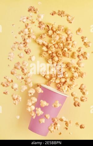 Fliegende köstliche süße Popcorn mit Karamell in rosa Papierbecher, isoliert auf Trendfarbe gelben Hintergrund.