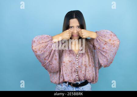 Schöne lateinische Frau trägt ein rosa Hemd über blau isoliert Hintergrund deprimiert und sorgen für Not, Weinen wütend und Angst. Trauriger Ausdruck. Stockfoto