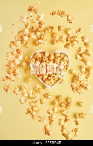 Fliegende leckere süße Popcorn mit Karamell in weißen Keramik-Herzteller, isoliert auf Trendfarbe gelben Hintergrund. Stockfoto