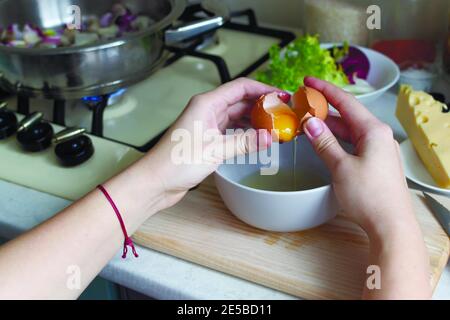 Eine Frau hält ein zerbrochenes Ei über einer Schüssel in ihrer Küche. Food-Blogger. Social-Media-Konzept. Horizontale Ausrichtung. Stockfoto