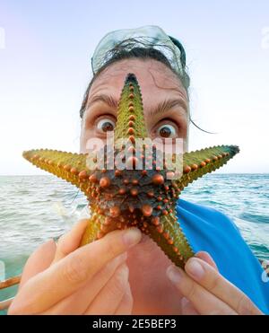 Weibchen zeigt einen grünen Seesterne und macht ein staunend überrascht Augen. Exotisches Urlaubskonzept. Stockfoto