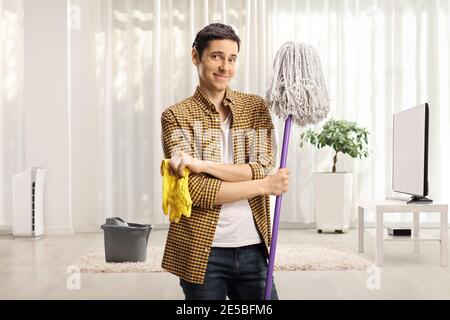 Junger Mann mit einem Putzmopp und einem Paar Handschuhe im Wohnzimmer Stockfoto