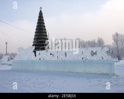 Der Name der Stadt auf Russisch aus Eis geschnitzt steht vor dem Hintergrund eines Weihnachtsbaumes mit dem Stadtwappen geschmückt. Stockfoto