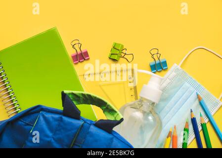 Schulbedarf mit medizinischer Maske und Desinfektionsflasche auf gelb Hintergrund.Selektiver Fokus Stockfoto