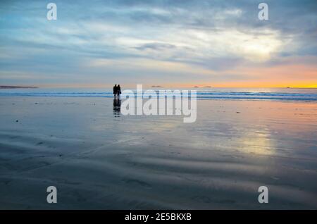 Junge Paar Silhouetten auf dem Silver Strand Beach nassen Sand beobachten den Sonnenuntergang auf Coronado Island, San Diego Südkalifornien USA. Stockfoto