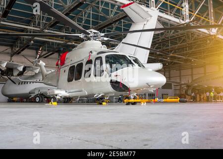 Passagierhubschrauber und Flugzeuge im Hangar. Rotorcraft und Flugzeuge unter Wartung. Mechanische Systeme für Flugbetrieb prüfen Stockfoto