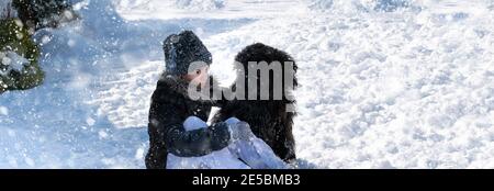 Mädchen mit schwarzen Golden-Doodle liegen auf Schnee im Winter Tag. Konzept der Hundefreundschaft. Leerzeichen für Text. Stockfoto