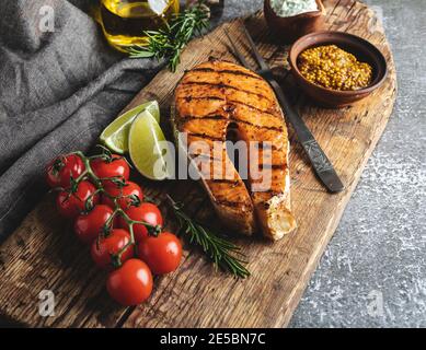 Gegrillter Steak Fisch Lachs, Forelle in einem alten Holzbrett, Gewürze, Rosmarin, Tomaten, Stockfoto