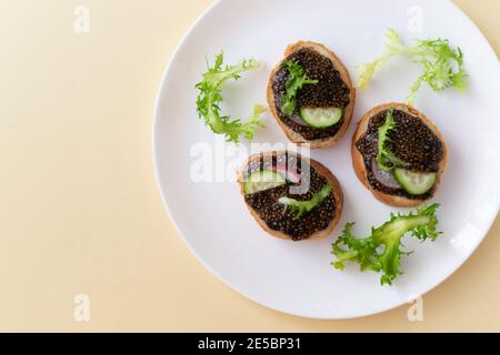 Chia Seed Sandwiches auf Baguette-Stücken mit Gurke, Rettich und Kräutern auf einem weißen Teller auf gelbem Grund. Gesunde Ernährung Konzept. Speicherplatz kopieren. Stockfoto