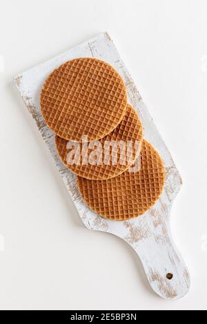 Draufsicht auf drei traditionelle holländische Stroopwafels (Sirup oder Karamellwaffeln) auf einem weißen Schneidebrett auf weißem Hintergrund, Kopierraum Stockfoto