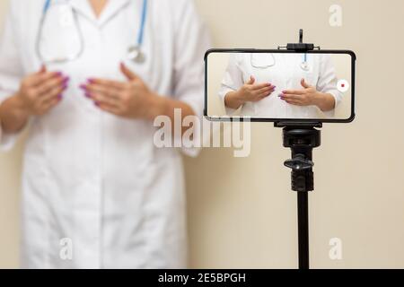 Ärztin Bloggerin, die Video auf einem Smartphone aufzeichnet, das auf einem Stativ steht. Stockfoto