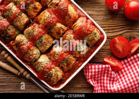 Hausgemachte Kohlrollen gefüllt mit Grütze und Pilze mit Tomaten Sauce in einer Auflaufform auf einer Holzplatte Anzeigen Stockfoto