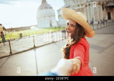 Lächelnd trendy Tourist Frau in Blumenkleid mit Hut erkunden Sehenswürdigkeiten mit Freund in der Nähe Cattedrale di Pisa. Stockfoto