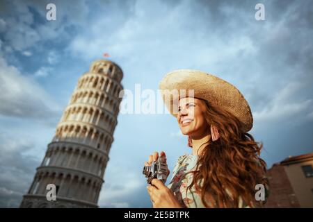 Glückliche trendige Frau mittleren Alters in Blumenkleid mit Retro-Kamera und Hut in der Nähe Schiefen Turm in Pisa, Italien. Stockfoto