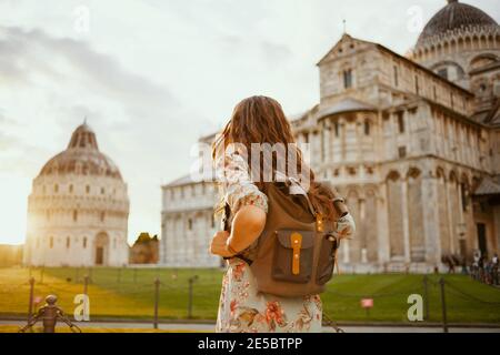 Von hinten gesehen moderne Reisende Frau in Blumenkleid mit Rucksack mit Ausflug in der Nähe der Kathedrale von Pisa. Stockfoto
