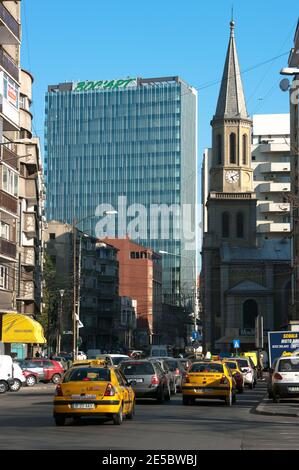 Bucarest, Rumänien - 21. April 2011: Kontrast zu einem neuen Wolkenkratzer und einem alten Glockenturm, dem Verkehr und gelben Taxis in einer Bukarest-Straße, Rumänien Stockfoto