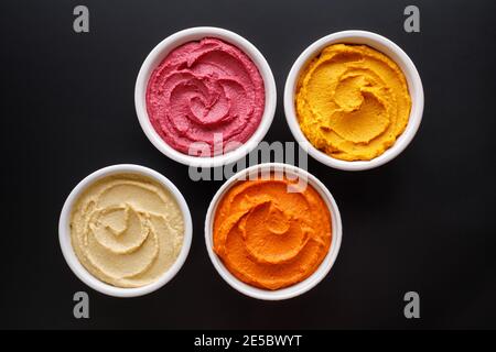 Ein Set Hummus aus verschiedenen Gemüsesorten in Keramikschalen auf schwarzem Hintergrund, Draufsicht Stockfoto