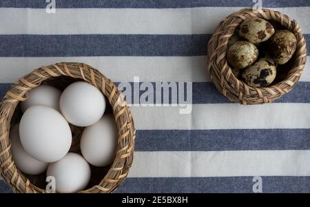 Weißes Huhn, Wachteleier in Körben und ein Handtuch auf einem weißen Holzhintergrund mit Platz für Text. Stockfoto