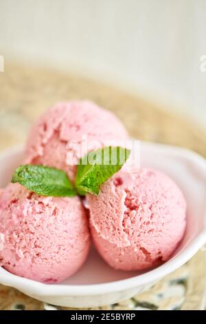 Erdbeereis mit Minzblatt. Drei Kugeln in einer weißen Schüssel auf einem Vintage-Tisch. Sorbet Stockfoto