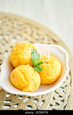 Mango-Eis mit Minzblatt. Drei Kugeln in einer weißen Schüssel auf einem Vintage-Tisch. Sorbet Stockfoto