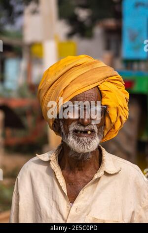 Nandakeshwar, Karnataka, Indien - 7. November 2013: Nahaufnahme eines alten Mannes mit großem safrangelbem Turban. Verloren Zähne und Sport dicken Rand Gläser. Stockfoto
