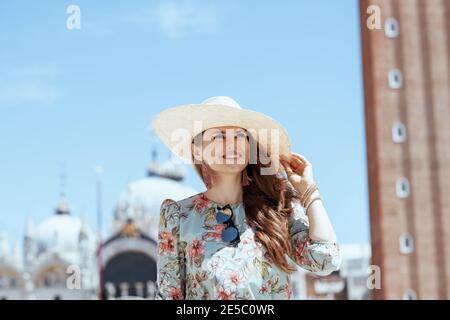 Happy stilvolle Solo-Tourist Frau in Blumenkleid mit Sonnenbrille und Hut mit Ausflug auf dem Markusplatz in Venedig, Italien. Stockfoto