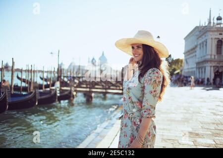 Happy stylish Frau in floralen Kleid mit Hut erkunden Attraktionen am Ufer in Venedig, Italien. Stockfoto