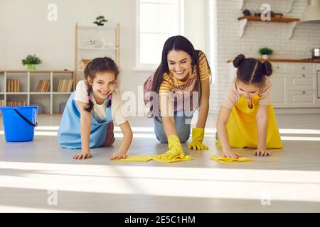 Eine glückliche junge Mutter und ihre charmanten kleinen Töchter wischen Der Boden zusammen Stockfoto