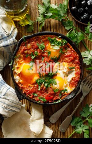 Traditionelles Shakshuka-Gericht, serviert in einer gusseisernen Pfanne auf einem Holztisch, Blick von oben Stockfoto