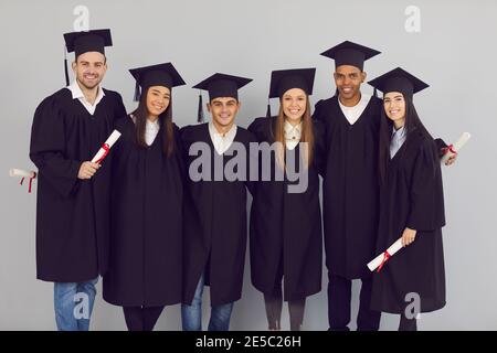 Gruppenportrait glücklicher multiethnischer Hochschulabsolventen oder Hochschulabsolventen, die sich umarmen Und Blick auf die Kamera Stockfoto