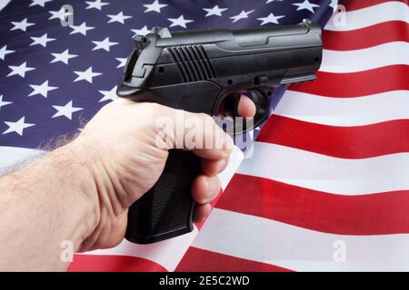 Pistole in der Hand eines Mannes vor dem Hintergrund der amerikanischen Flagge, selektiver Fokus. Stockfoto