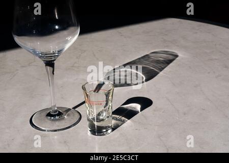Tisch aus Kunstmarmor auf der Restaurantterrasse nach dem Abendessen mit Leeres Weinglas und leerer Vorspeise Ouzo Schnaps Glas mit Schöner Schattenhoriz Stockfoto