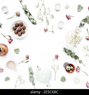 Arbeitsbereich mit Rosenknospen, Eukalyptus-Blätter, saftig, Tee, Tasse Kakao, Süßigkeiten auf weißem Hintergrund. Flach liegend, Ansicht von oben, Arbeitsplatz im Home Office Stockfoto