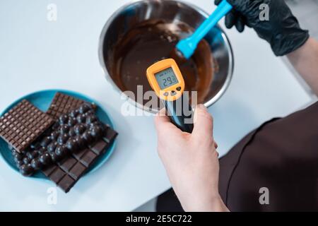 Nahaufnahme der weiblichen Temperaturmessung von geschmolzener Schokolade mit Pyrometer Stockfoto