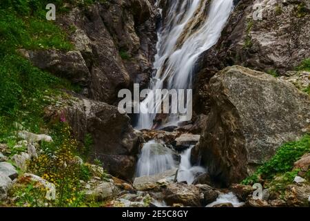 Wasserfall zwischen Felsen mit Blumen und Pflanzen an der Seite Im Sommer Stockfoto