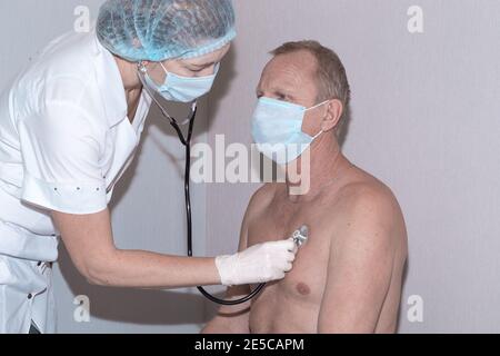 Eine Ärztin mit Phonendoskop hört einem reifen Mann zu. Gesundheitscheck vor der Coronavirus-Impfung. Stockfoto