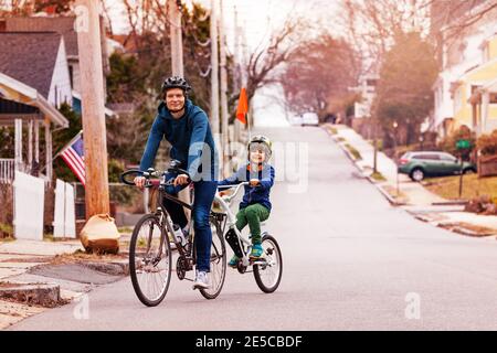 Kleiner glücklicher Junge Fahrt auf einem Schlepptandemrad mit Flagge am Vater auf der städtischen Straße angebracht Stockfoto