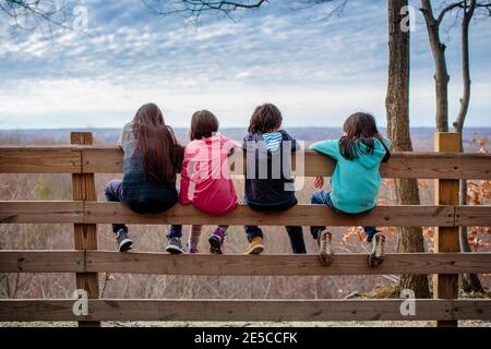 Vier Kinder sitzen ruhig zusammen am Zaun und blicken hinüber Ein Tal Stockfoto