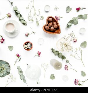 Arbeitsbereich mit Rosenknospen, Eukalyptus-Blätter, saftig, Tee, Tasse Kakao, Süßigkeiten auf weißem Hintergrund. Flach liegend, Ansicht von oben, Arbeitsplatz im Home Office Stockfoto