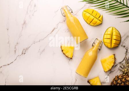 Frischer tropischer Smoothie mit Ananas und Mango in Flaschen auf Marmorboden. Draufsicht. Leerzeichen für Text. Stockfoto