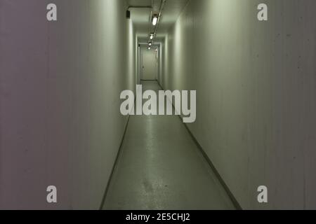 Langer, enger und leerer Flur auf Augenhöhe mit gelb-grünlichem Licht Stockfoto