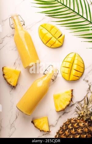 Frischer tropischer Smoothie mit Ananas und Mango in Flaschen auf Marmorboden. Draufsicht. Stockfoto